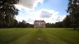 A large brick building with a red roof, surrounded by a grassy field and trees.