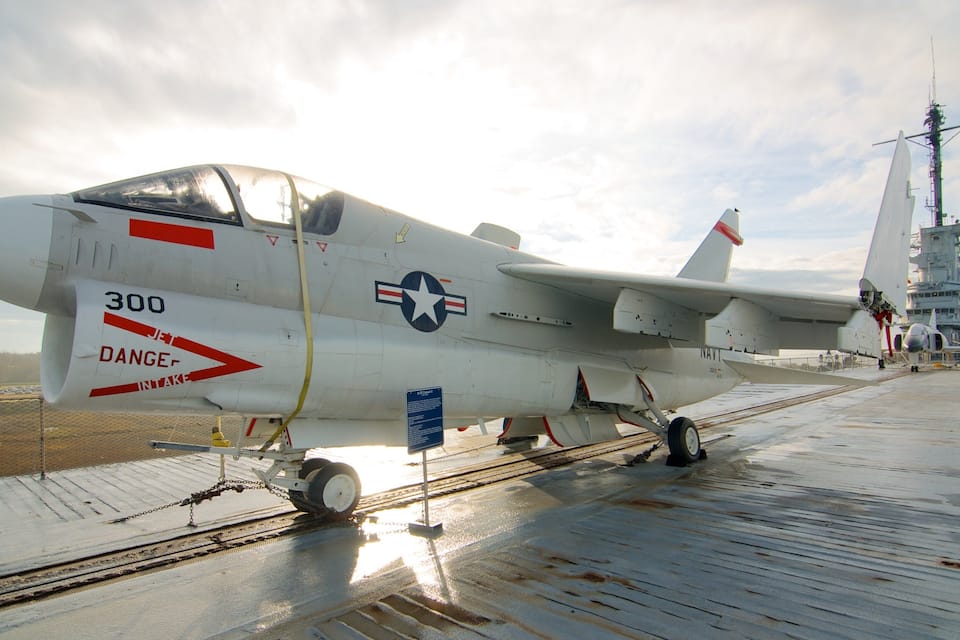 Un avion militaire portant le numéro 300 sur son fuselage, stationné sur un pont d’envol, avec un navire en arrière-plan.