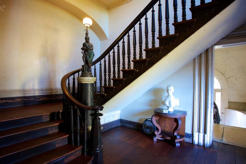 A grand staircase with dark wooden balusters and a white marble base. A bust sculpture is placed on a pedestal near the bottom of the stairs.