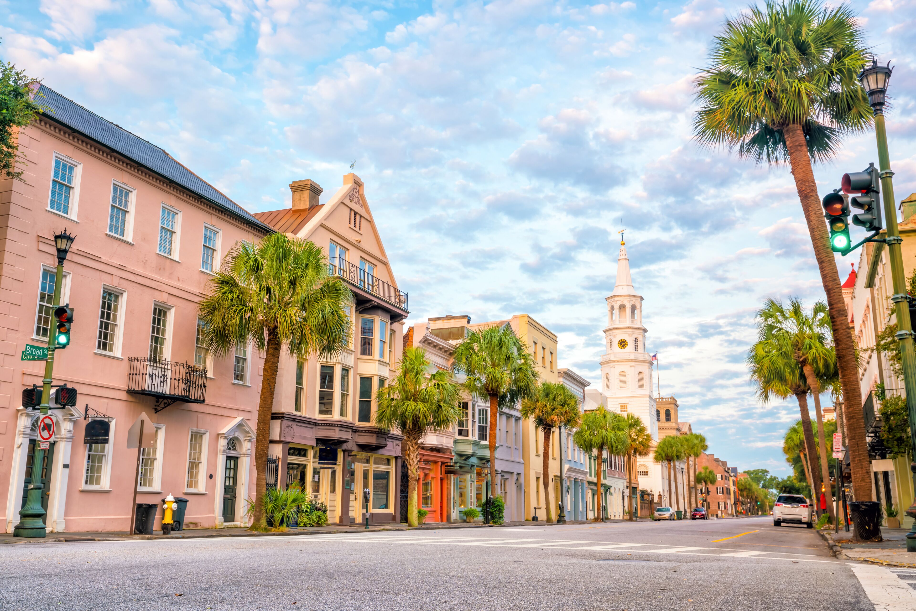 A historic street lined with palm trees and buildings, including a church with a steeple.