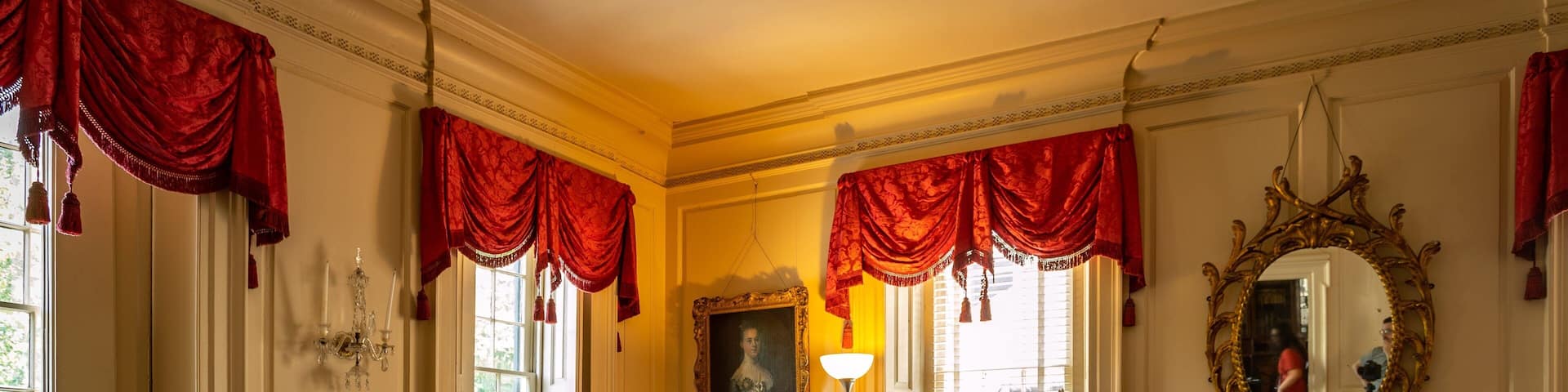 A room with ornate furniture, red drapes, a large mirror, and a piano.