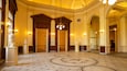 Un salón imponente con puertas de madera ornamentadas, estatuas clásicas y una alfombra estampada.