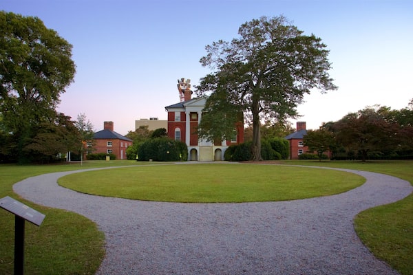A large red brick building with a central entrance, surrounded by a circular gravel path and lush green trees.