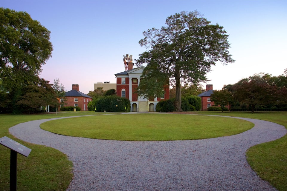 A large red brick building with a central entrance, surrounded by a circular gravel path and lush green trees.