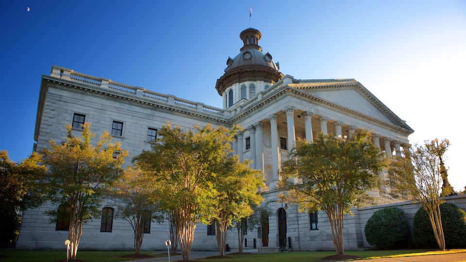 A large neoclassical building with a prominent dome and columns, surrounded by trees and a clear sky.