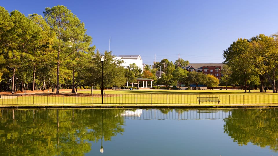 A park with a pond, trees, a gazebo, and buildings in the background.