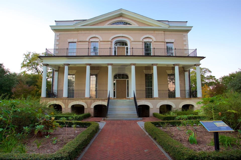 A large, two-story building with a central entrance flanked by columns, surrounded by a brick pathway and greenery.