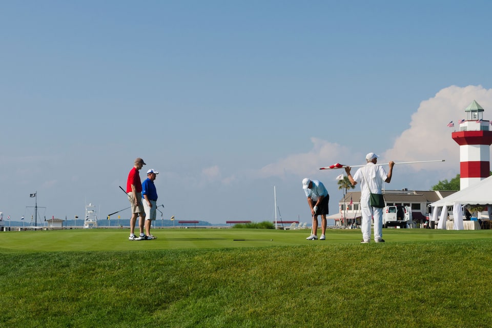 Un campo de golf con jugadores, un faro y cielo despejado.