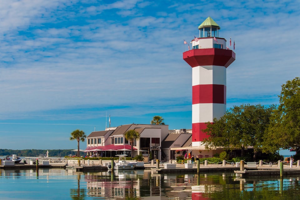 Un faro rojo y blanco, un puerto deportivo con barcos y un edificio con toldo rojo.