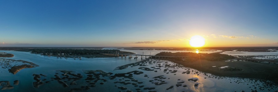 Un coucher de soleil sur une rivière, avec des îles et un pont.