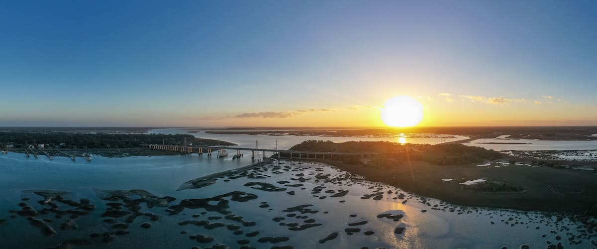 A sunset over a river with islands and a bridge.