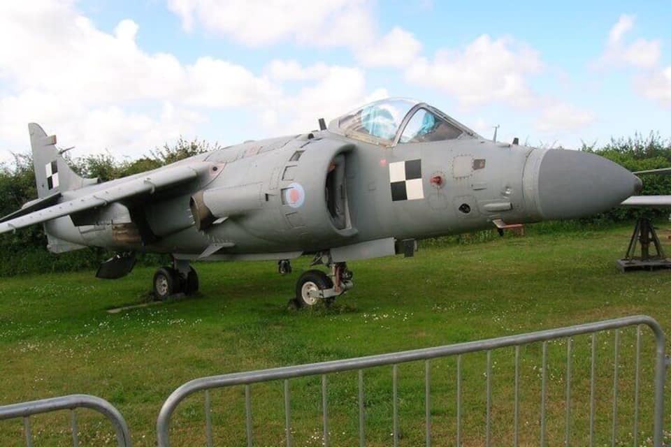 Un avion militaire est exposé dans un champ verdoyant, sous un ciel dégagé.