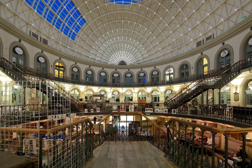 A grand, multi-level shopping mall with ornate railings and a high, glass-domed ceiling.