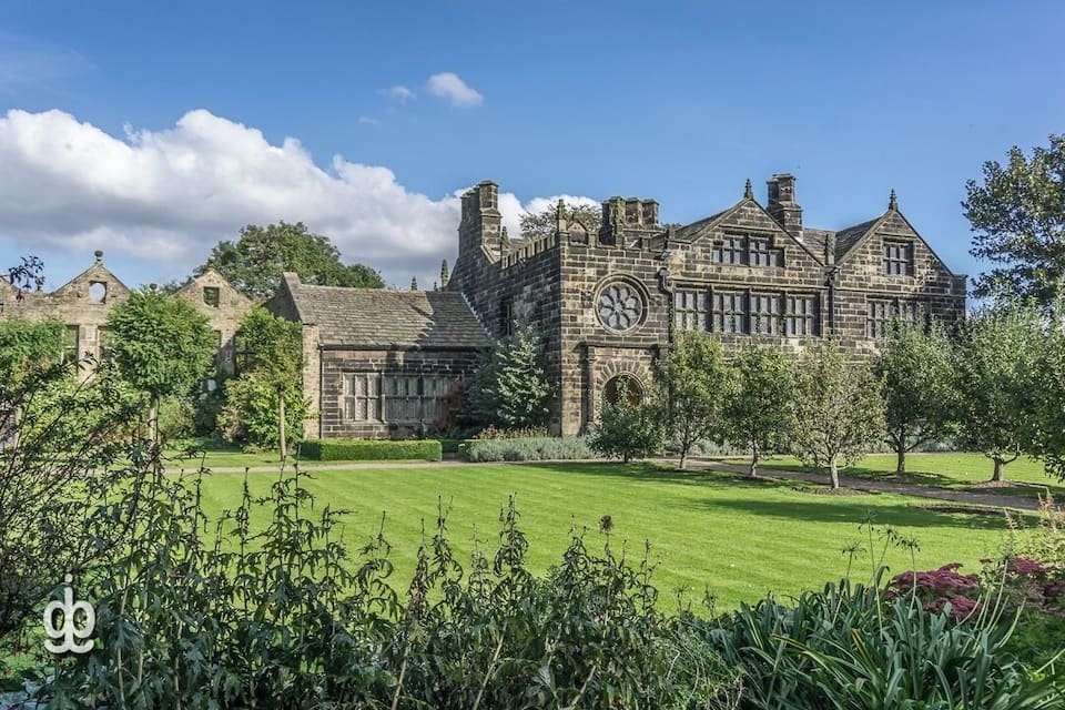 A large stone building with a clock tower, surrounded by a well-maintained lawn and trees.