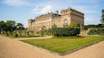 A large, historic building with a formal garden and well-manicured lawns.