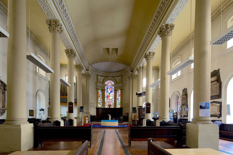 A church interior with high ceilings, ornate columns, and a central stained glass window.