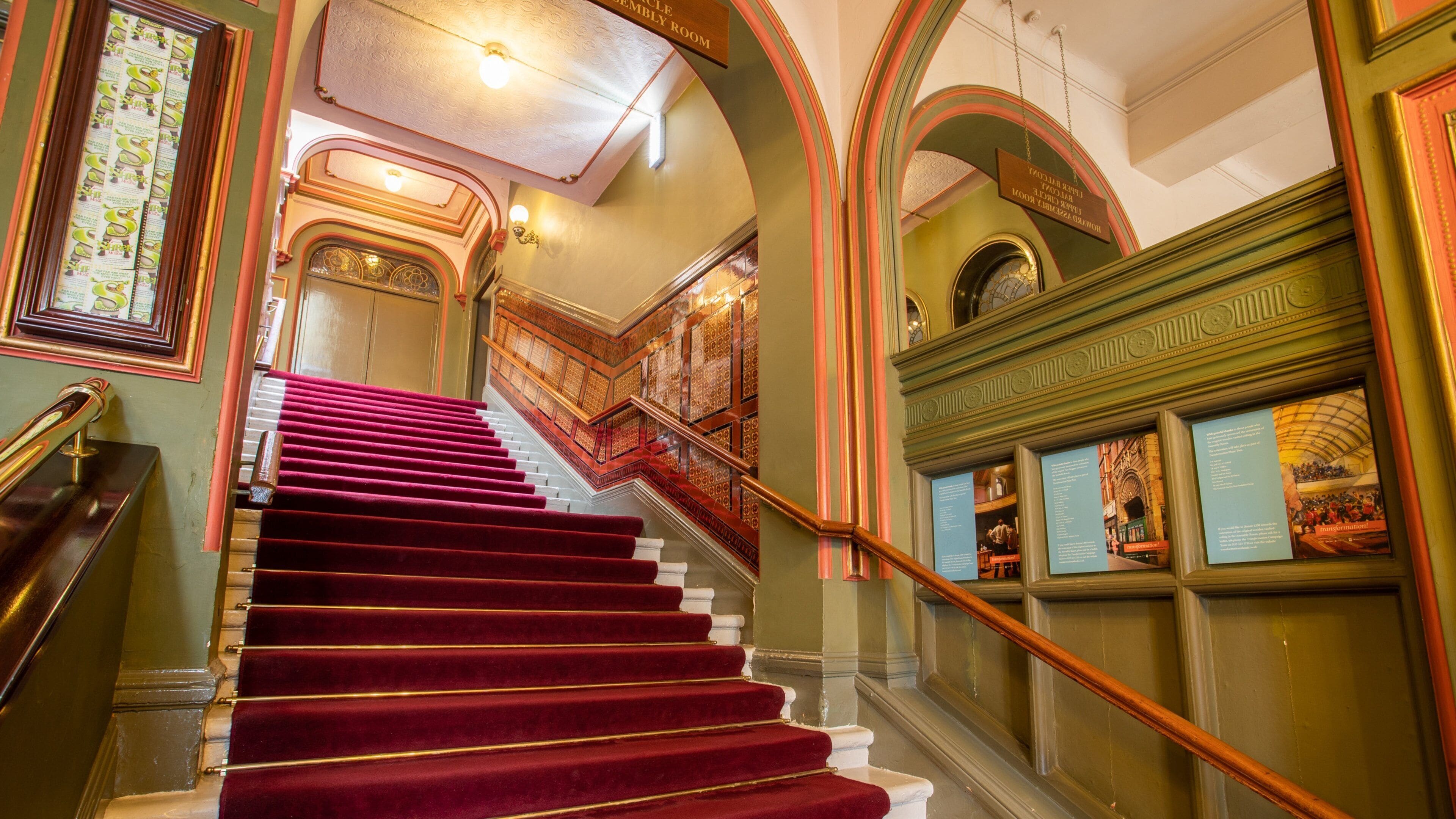 A grand staircase with red carpeted steps, ornate railings, and decorative moldings.