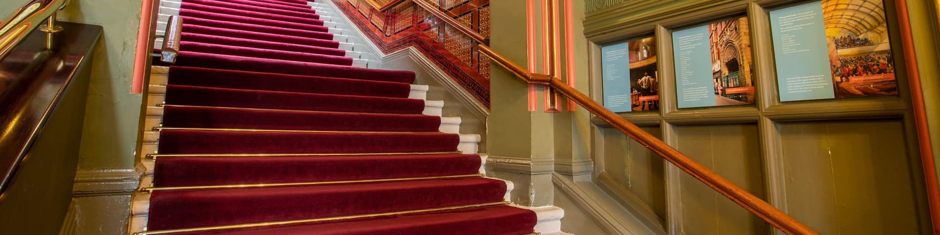 A grand staircase with red carpeted steps, ornate railings, and decorative moldings.