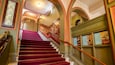 A grand staircase with red carpeted steps, ornate railings, and decorative moldings.