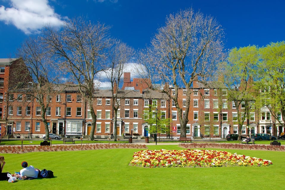 A park with a flower bed and red brick buildings in the background.