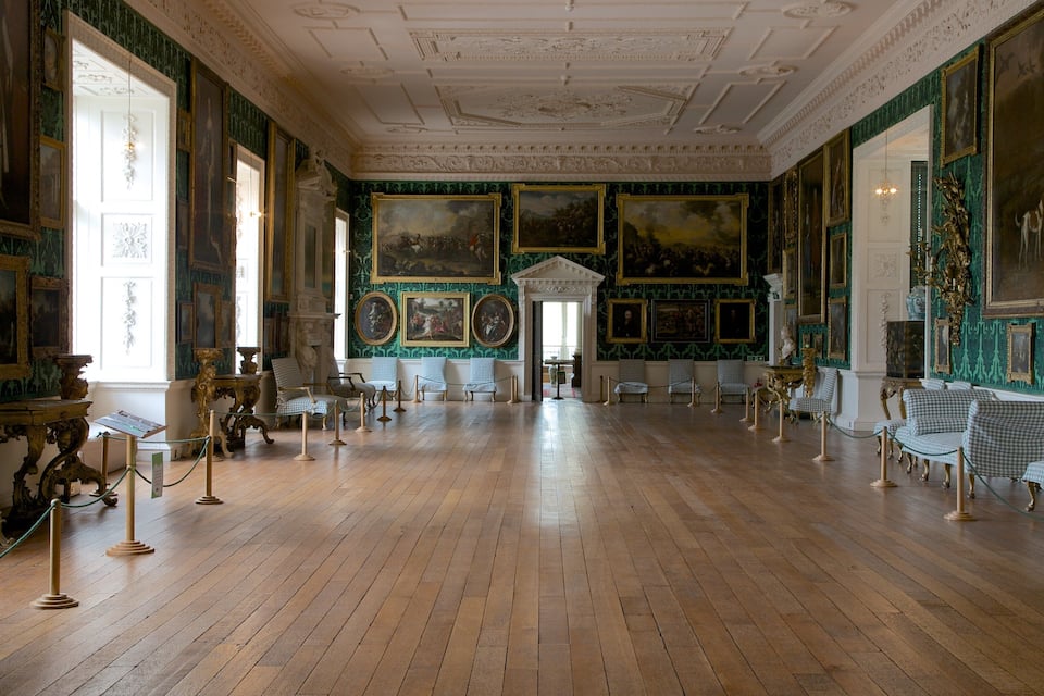 A grand room with ornate furniture, green patterned wallpaper, and classical paintings.