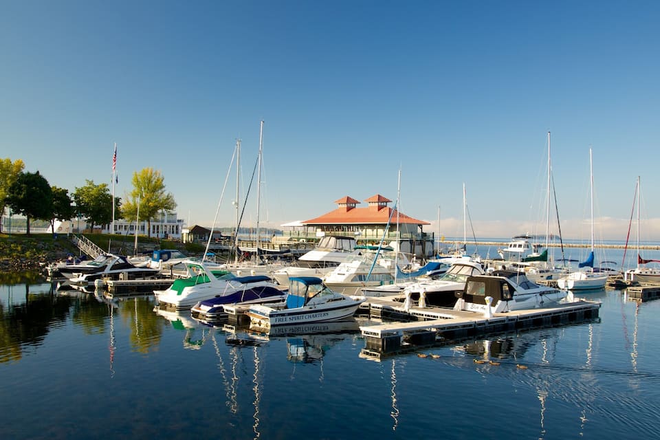 A marina with various boats docked, a building with a red roof, and trees along the water's edge.