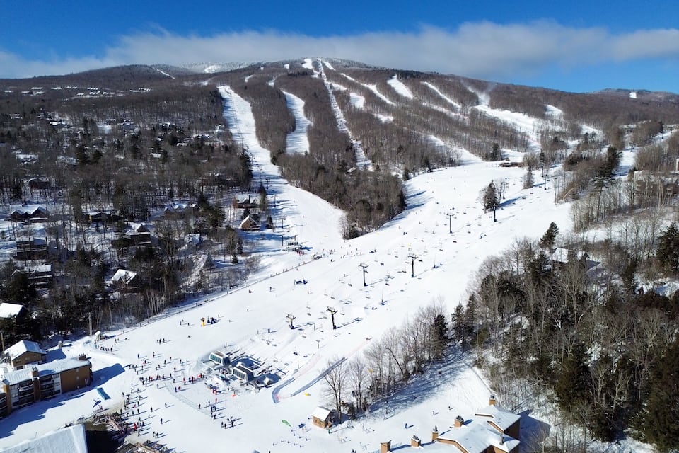 A snow-covered ski resort with ski lifts, buildings, and a mountain backdrop.