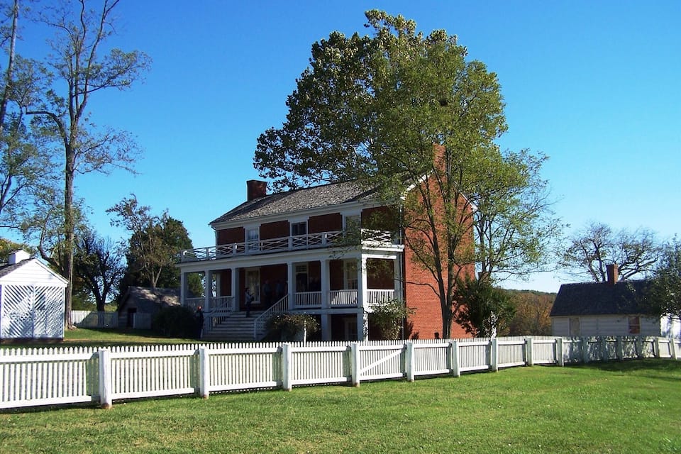A large, two-story brick house with a white porch and a white picket fence.