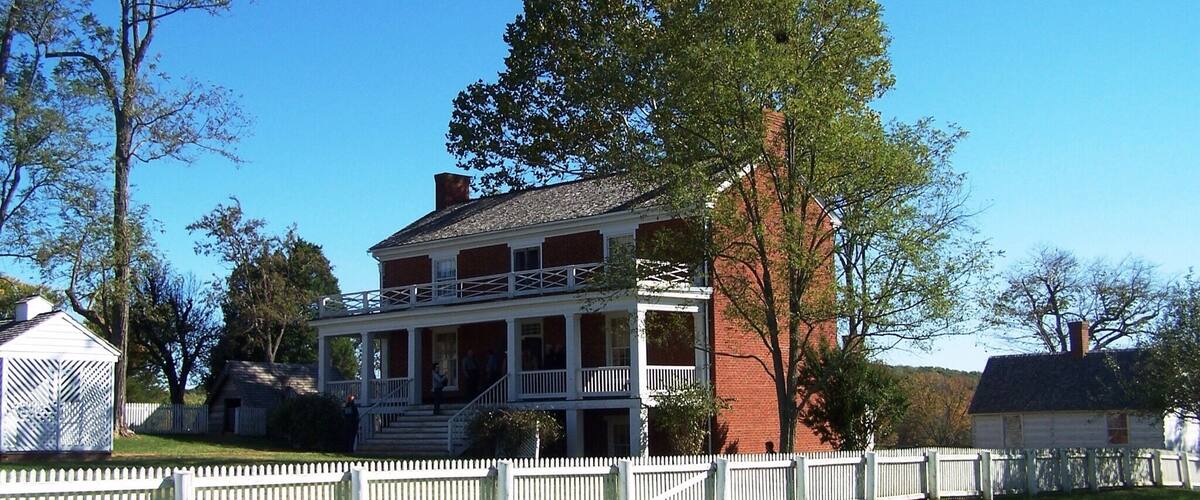 A large, two-story brick house with a white porch and a white picket fence.