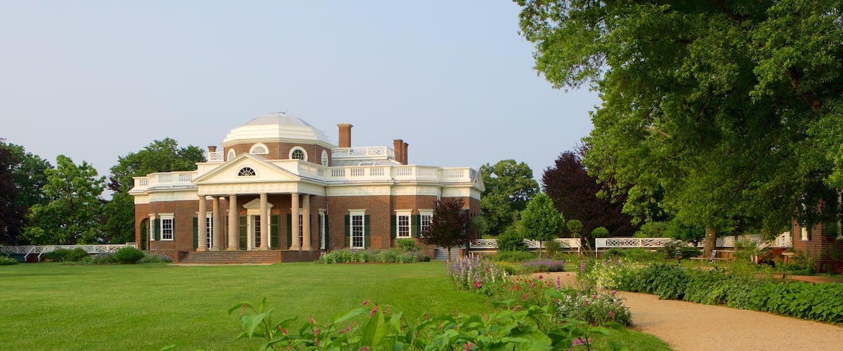 A large brick building with a dome and columns, surrounded by a well-maintained garden with various plants and flowers.