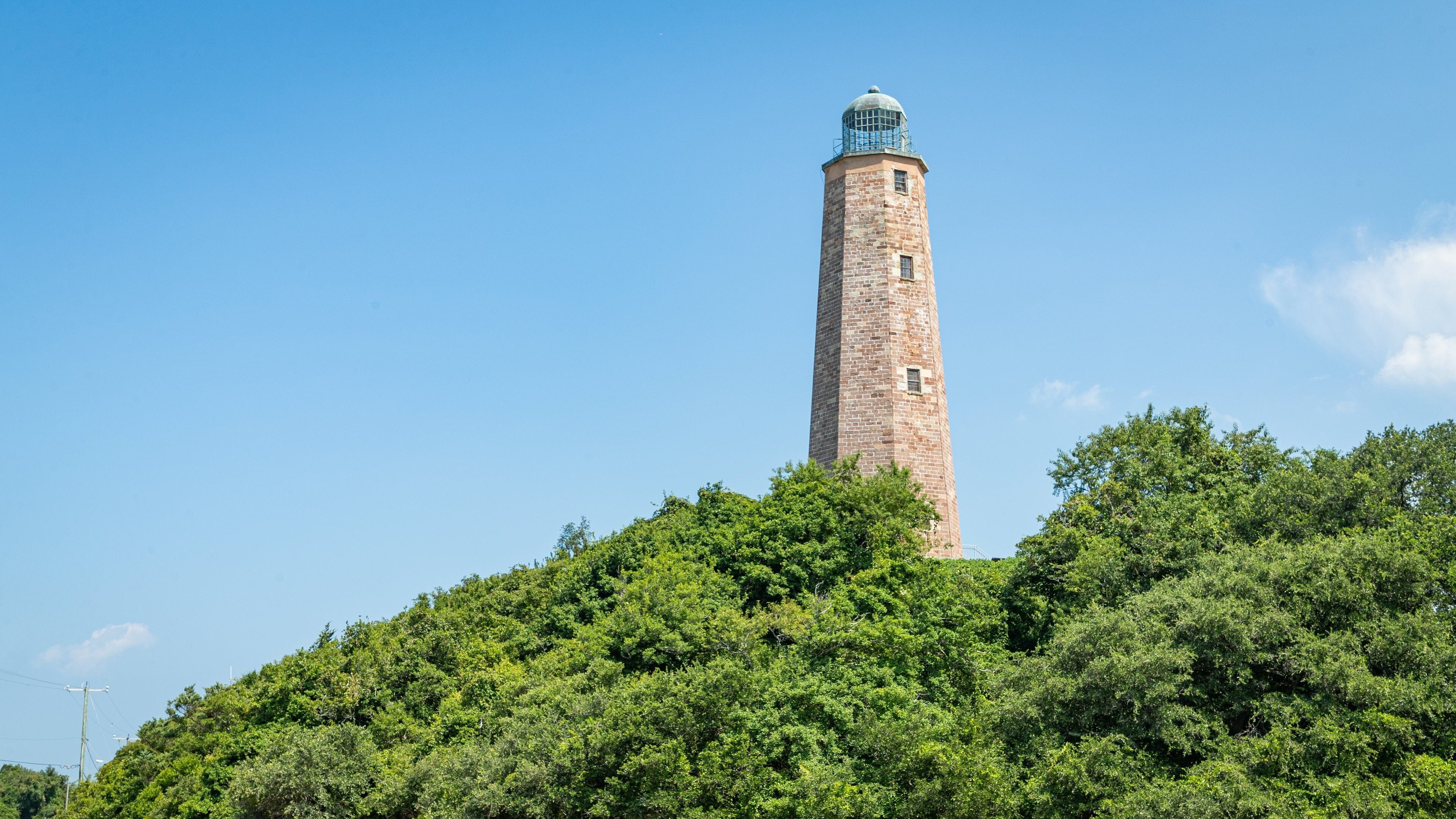 A tall brick tower with a dome on top, surrounded by dense green trees.