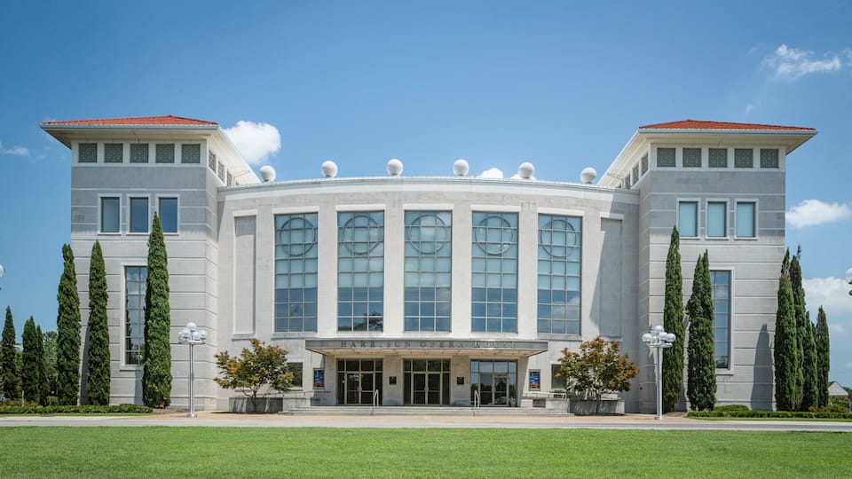 A large, modern building with a curved facade, large windows, and a red-tiled roof.
