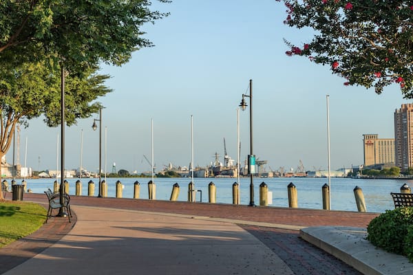 Une promenade au bord de la rivière, agrémentée de bancs, d’arbres et offrant une vue sur les bâtiments industriels et les grues qui se dressent de l’autre côté de l’eau.