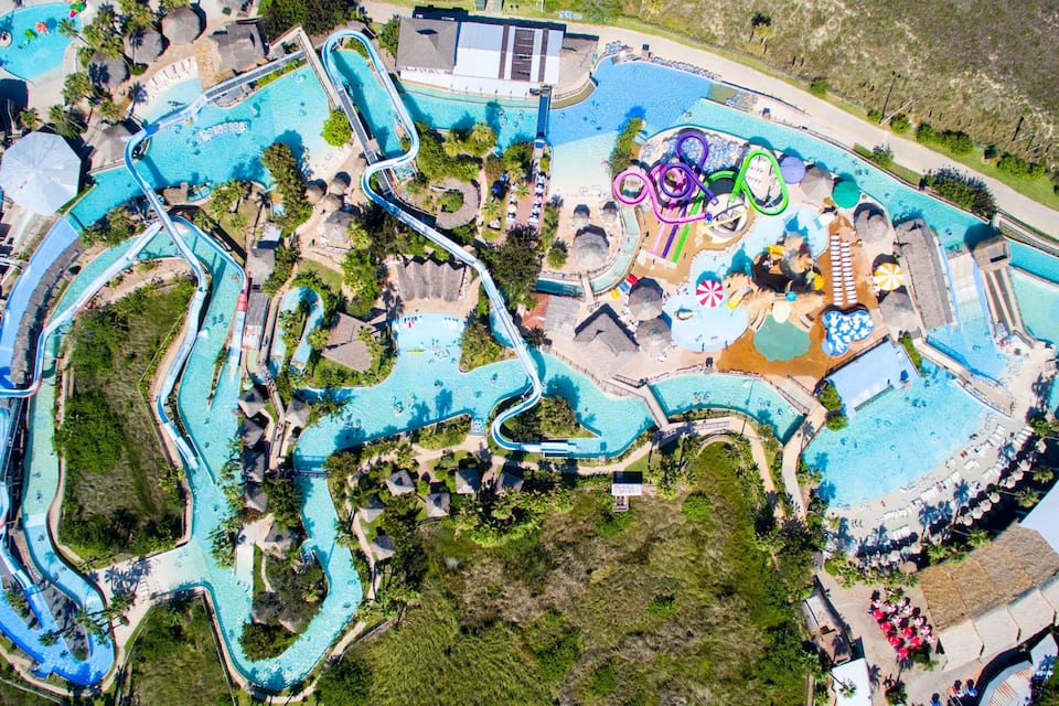 En vy från ovan över en vattenpark med slingrande vattenrutschkanor, flera pooler och ett stort sandområde.