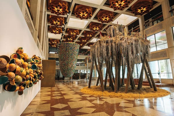 Une installation artistique comprenant des pièces de poterie et des branches suspendues, le tout installé dans un vaste espace intérieur doté d’un sol à motifs et d’un plafond haut.