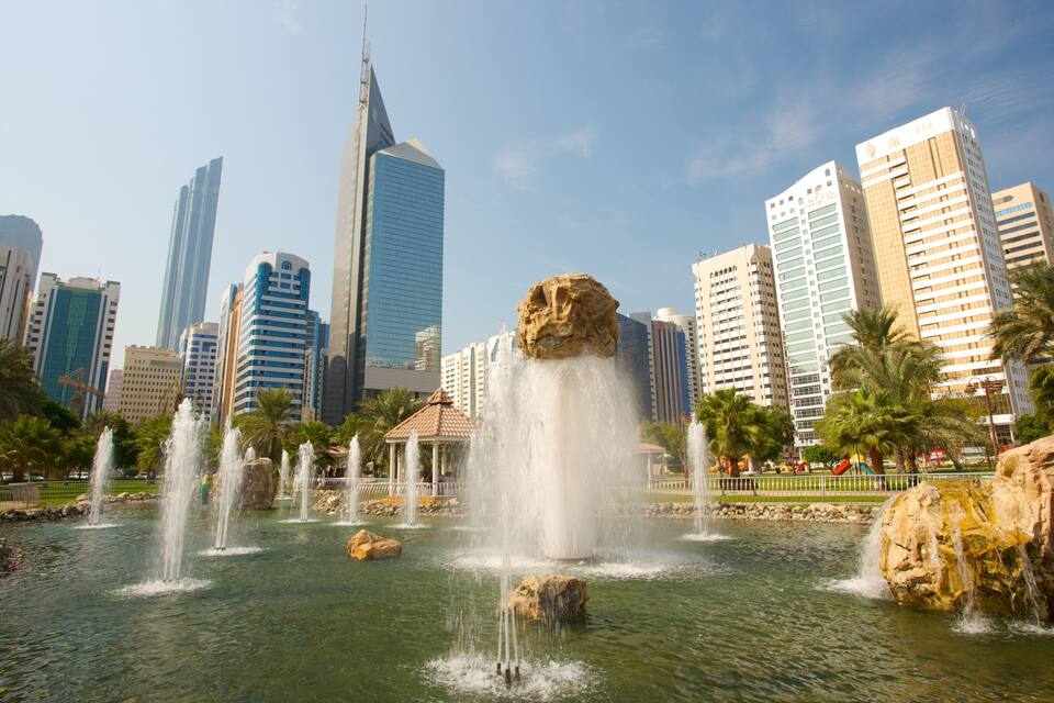 A cityscape with modern skyscrapers and a central fountain with water jets.