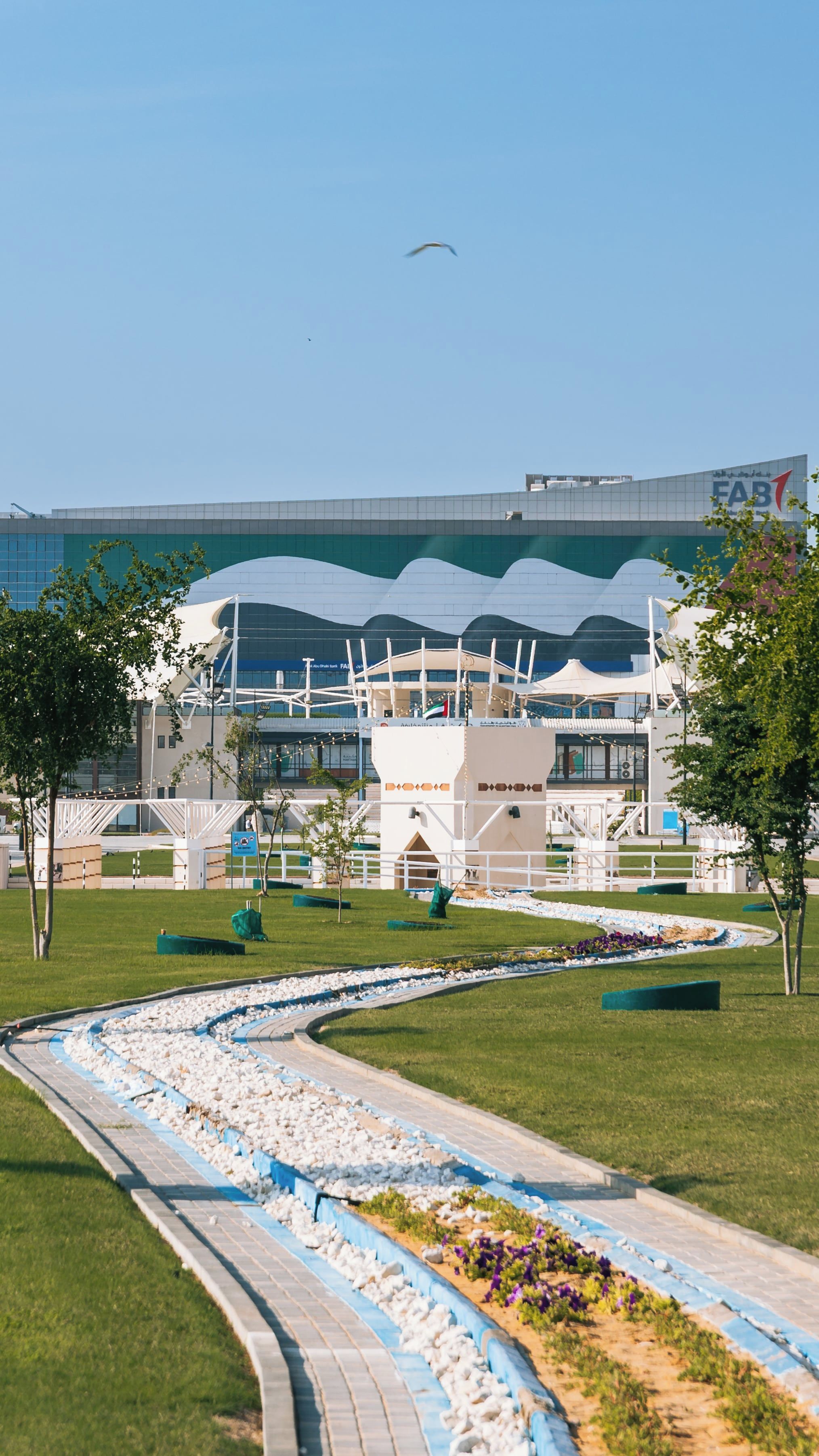Estadi modern amb teulada corbada, envoltat de jardins paisatgístics i un camí sinuós.