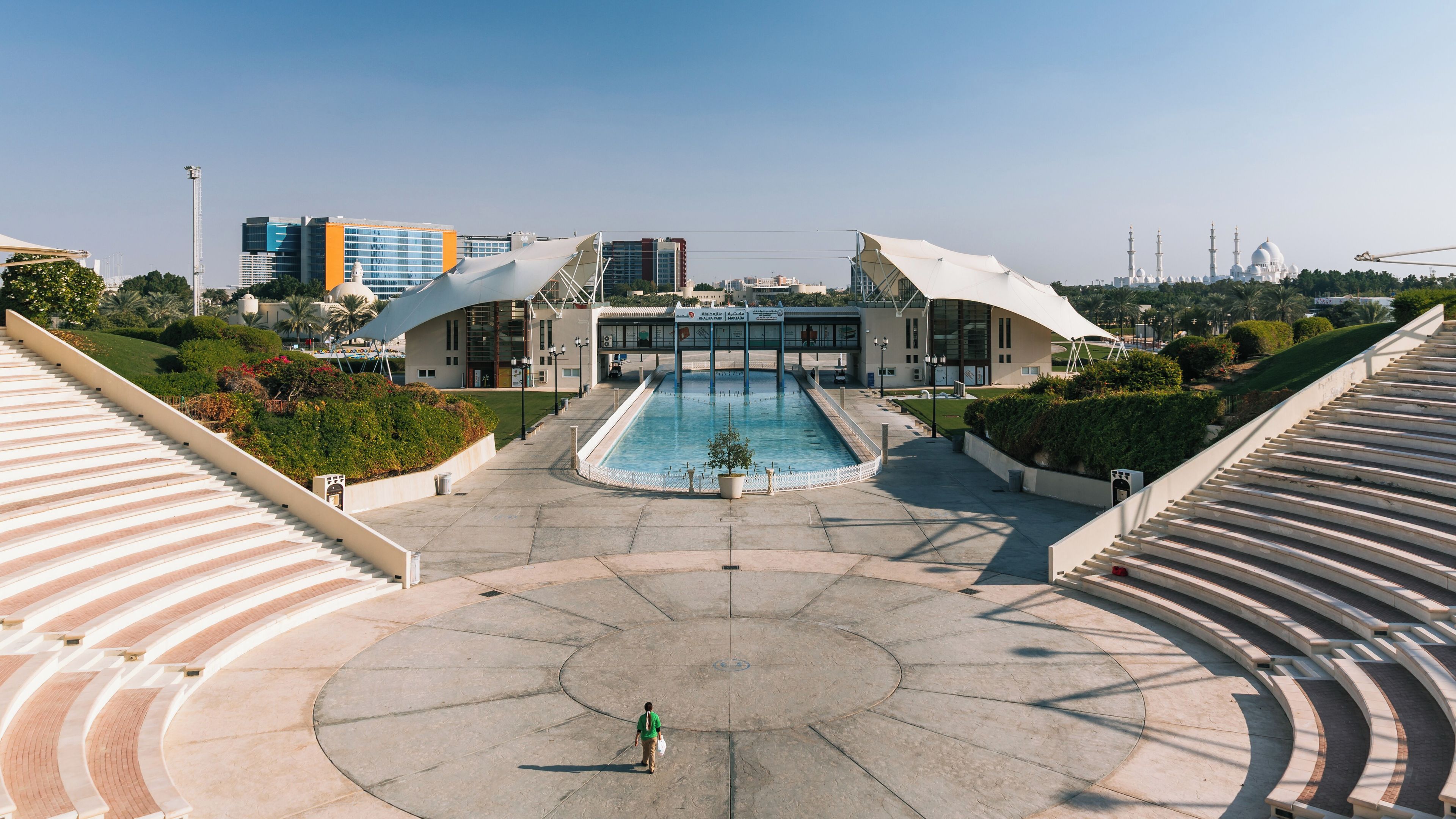 Una gran plaça oberta amb una piscina central, envoltada d'edificis moderns i una gran mesquita al fons.