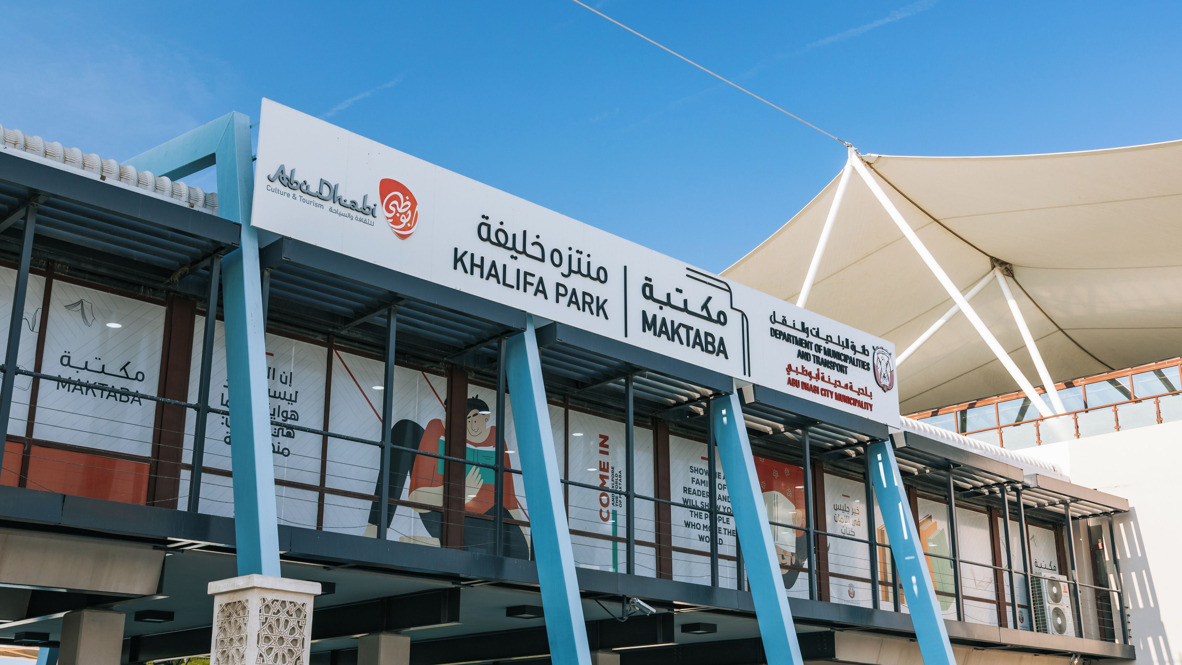 Un edificio moderno con señalización para Khalifa Park y Maktaba, que incluye texto en árabe y un logotipo.