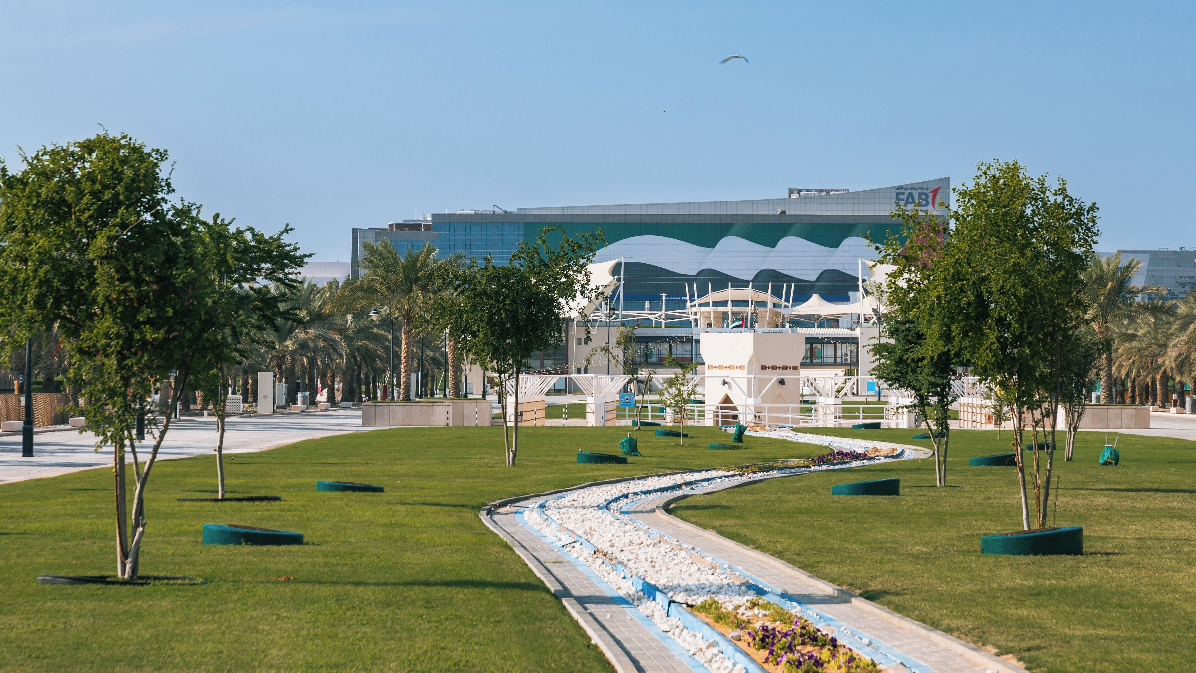 Un edifici modern amb una façana corba singular, envoltat d'un parc ben cuidat amb arbres i un camí paisatjístic.