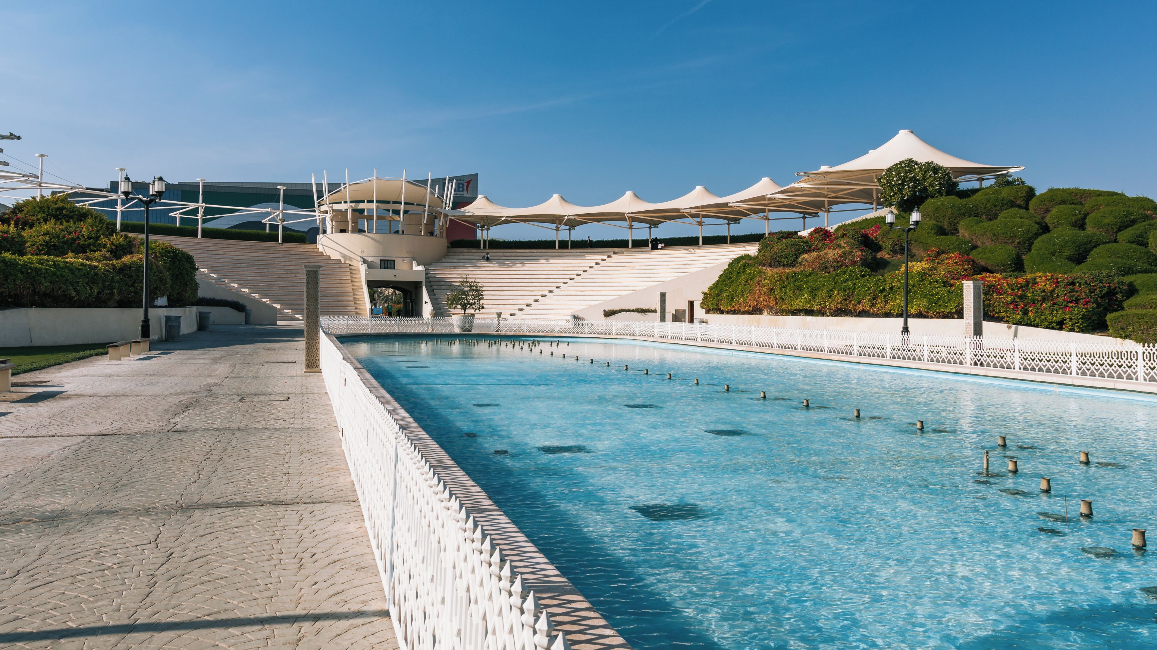 Una gran piscina amb una tanca blanca, una zona d'estar coberta i un edifici amb estructura de cúpula.
