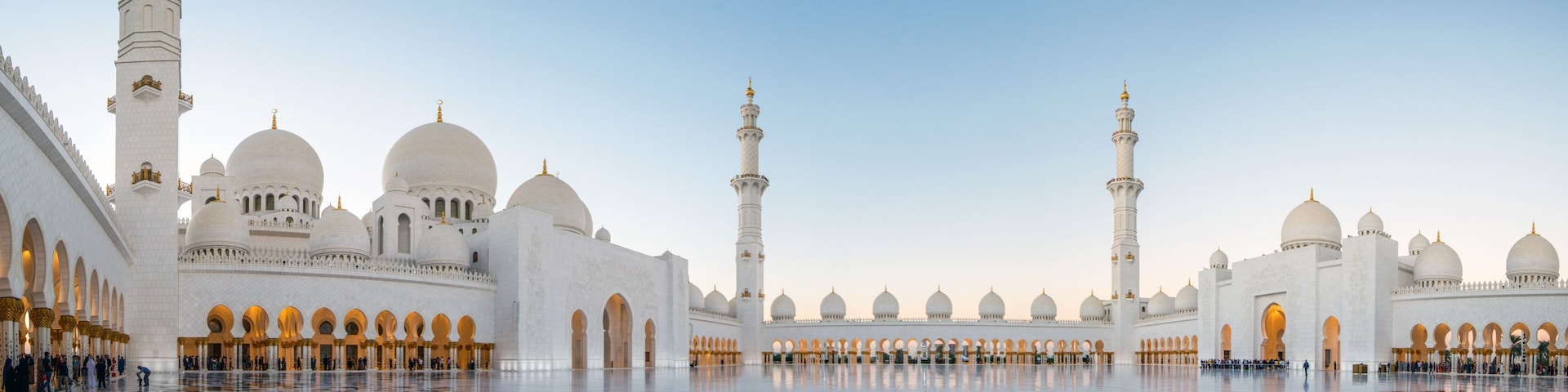 A large mosque with multiple domes and minarets, a spacious courtyard with intricate tile work, and a clear sky.