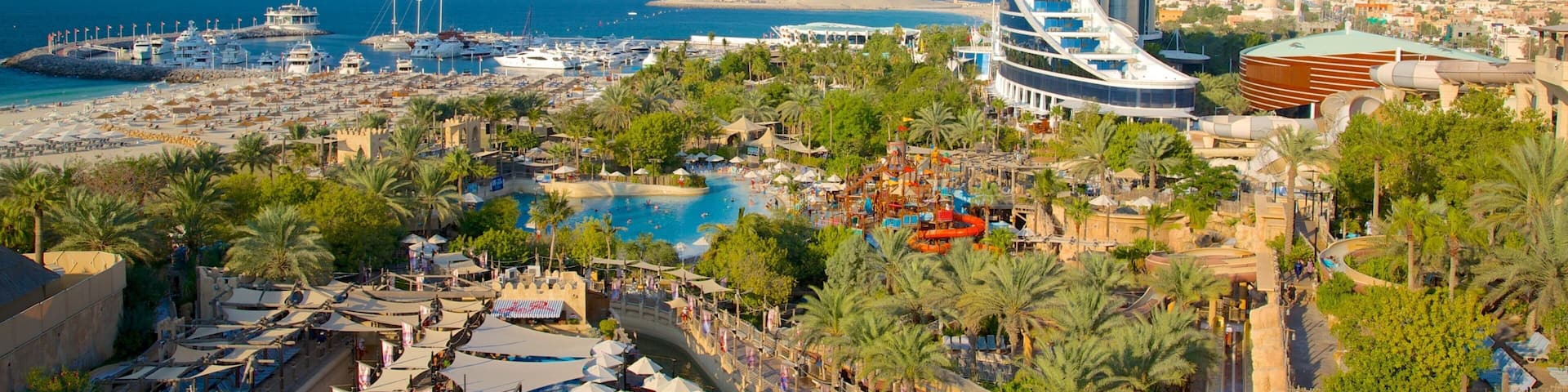 A coastal resort with a distinctive sail-shaped building, a marina with yachts, and a large pool area.
