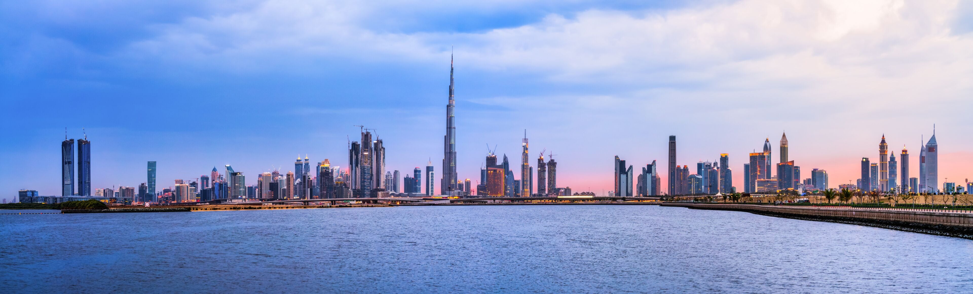 A city skyline with a prominent skyscraper, a river in the foreground, and a bridge connecting two land masses.