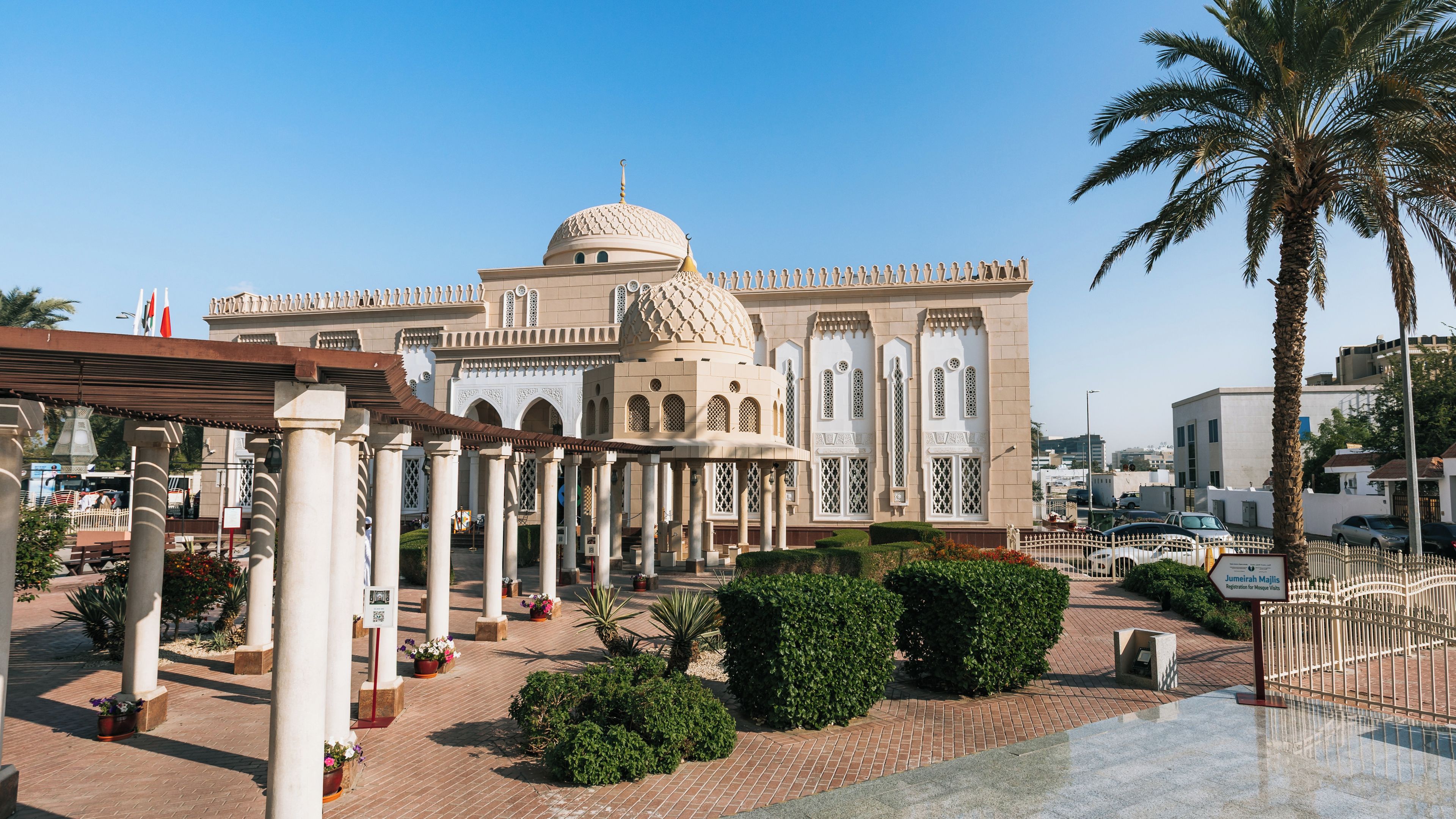 A mosque with a large dome and arched windows, surrounded by palm trees and a paved walkway.