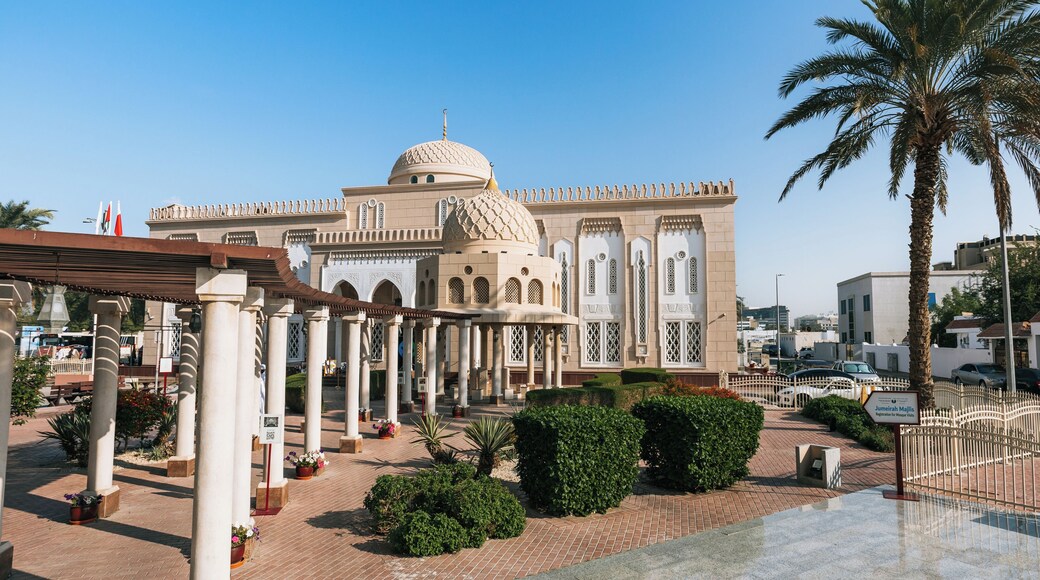 A mosque with a large dome and arched windows, surrounded by palm trees and a paved walkway.