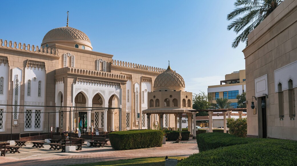 A mosque with domes and arches, a paved courtyard, and benches.