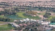 Aerial view to Golf course with green lawn and lakes, villa houses behind it timelapse.