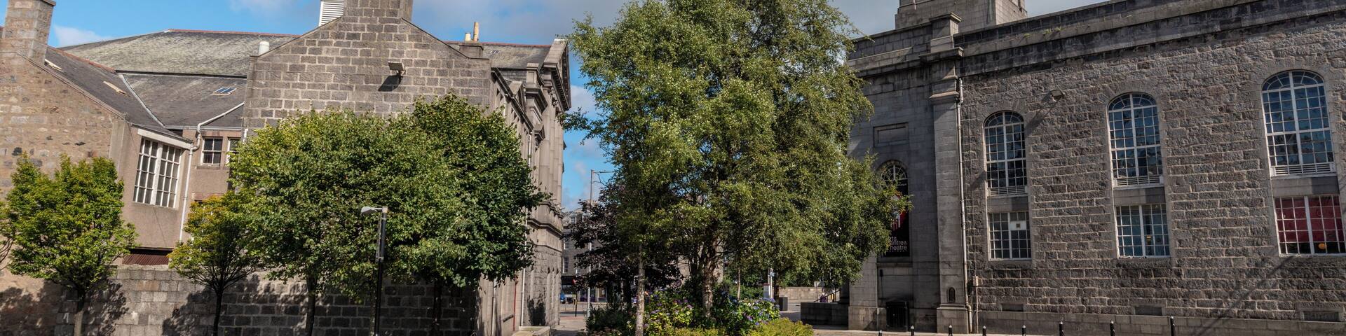 A historic building with a clock tower, stone walls, and trees.