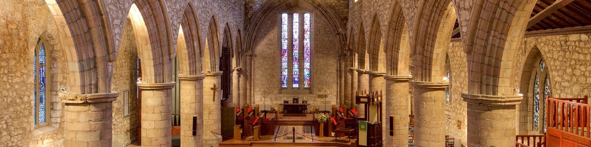 A cathedral interior with stone arches, wooden pews, and stained glass windows.